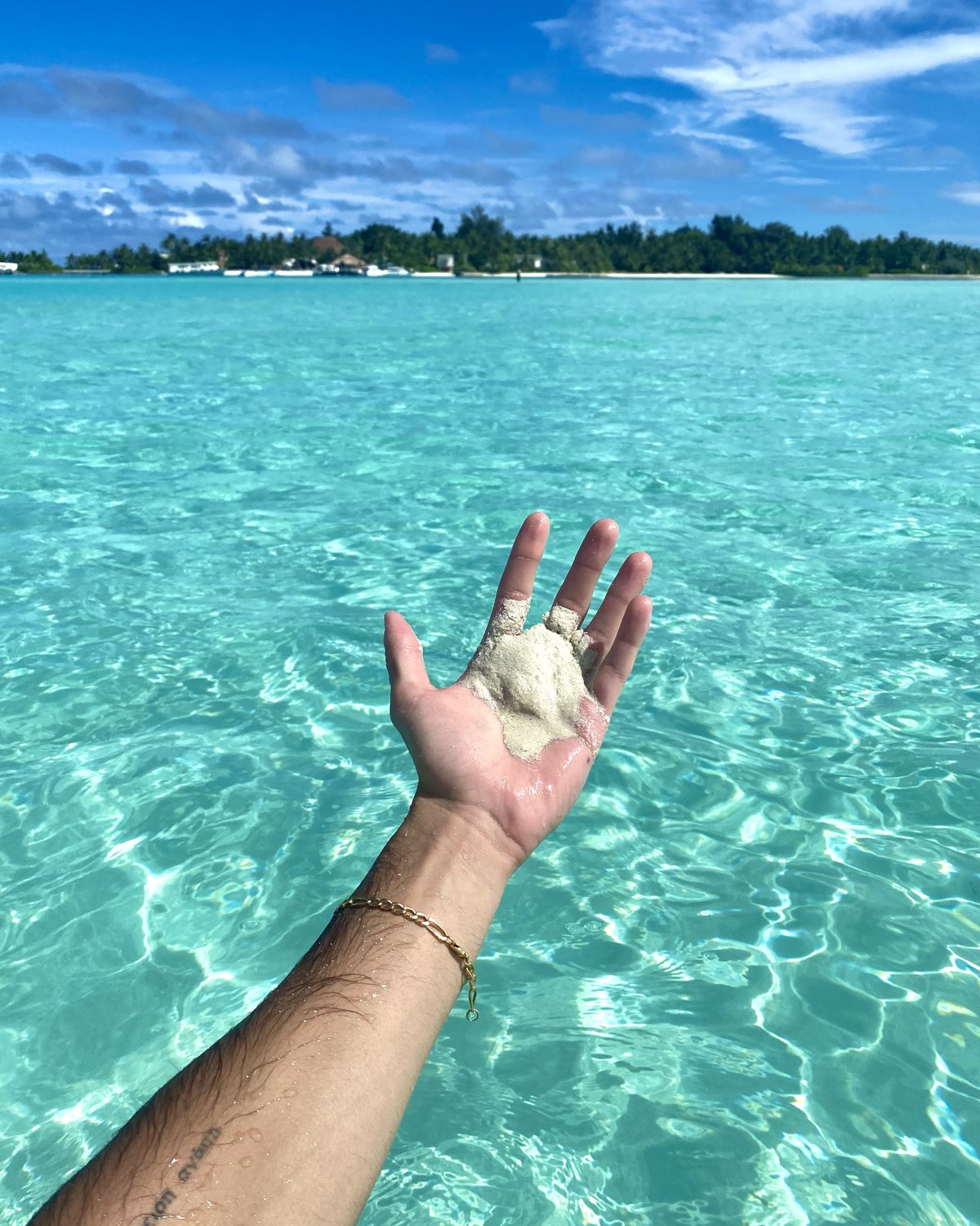 Una mano sosteniendo un puñado de arena sobre el agua transparente de un cayo