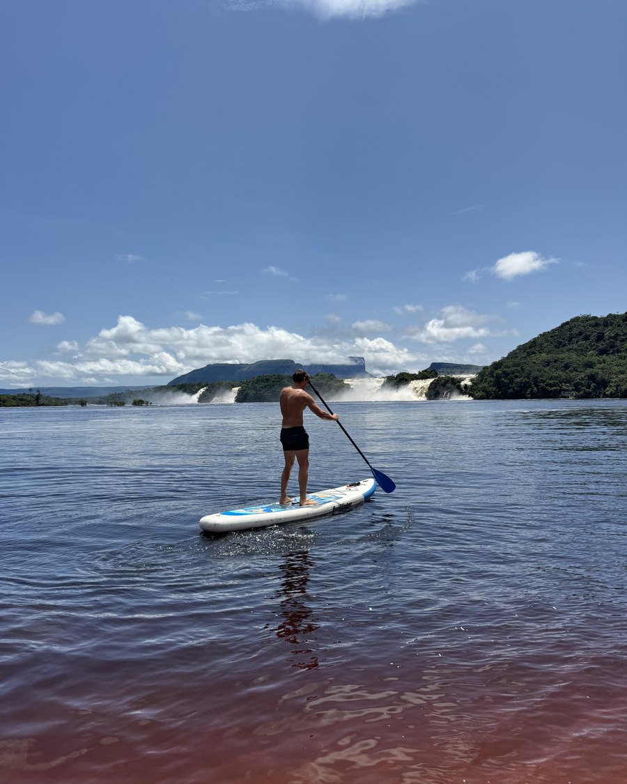 Alguien remando de pie en la laguna de Canaima, con los saltos al fondo